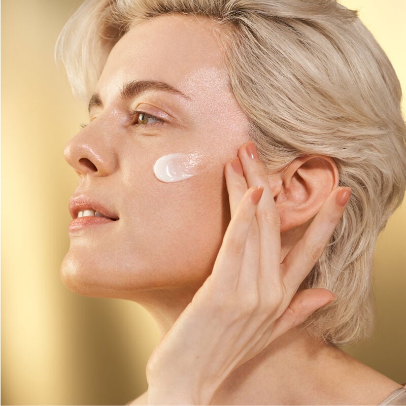 A model gently applying the Shiseido Vital Perfection Uplifting and Firming Advanced Cream to her upper left cheekbone.