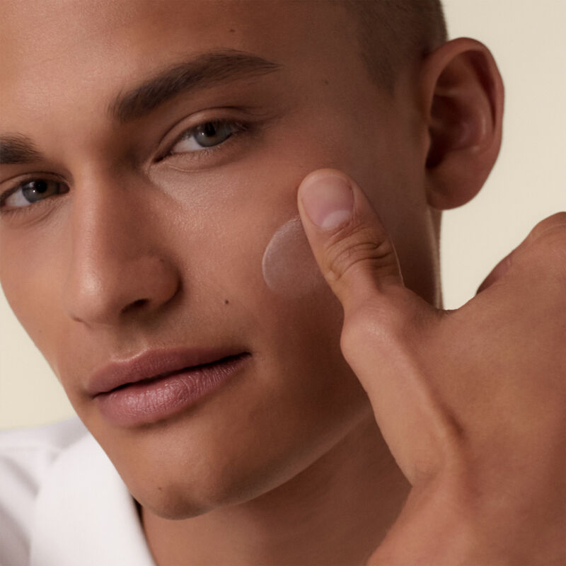 A male model applying the Shiseido Urban Environment Oil-Free Sunscreen SPF 42 against his cheek, showcasing its creamy application.