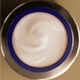 Un frasco redondo, open jar of Shiseido Vital Perfection Uplifting and Firming Advanced Cream from above, filled with a light cream-colored product swirled inside.
