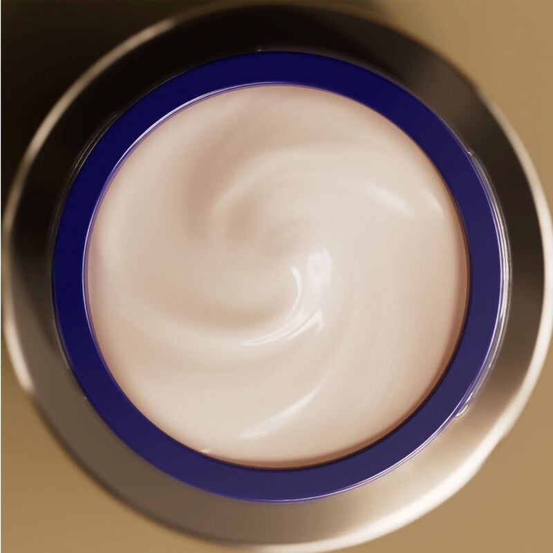 Un frasco redondo, open jar of Shiseido Vital Perfection Uplifting and Firming Advanced Cream from above, filled with a light cream-colored product swirled inside.