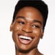 "A headshot of a model wearing the Shiseido Revitalessence Skin Glow Foundation SPF 30 in shade 510 Suede. The models’ skin appears more smooth and glowy with the foundation's medium-coverage finish.  "
