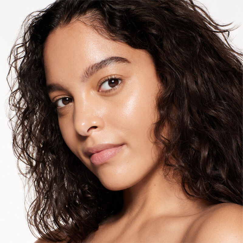 "A headshot of a model wearing the Shiseido Revitalessence Skin Glow Foundation SPF 30 in shade 340 Oak. The models’ skin appears more smooth and glowy with the foundation's medium-coverage finish.  "