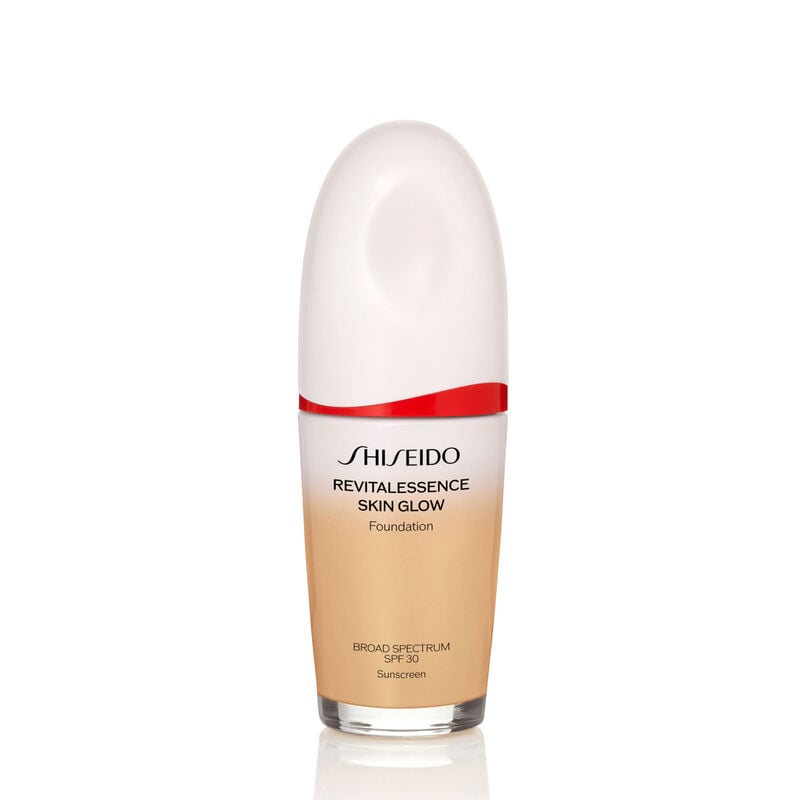 "An oval-shaped bottle of Shiseido Revitalessence Skin Glow Foundation SPF 30 in shade 340 Oak. The label on the bottle is white with a red accent. El texto en la etiqueta muestra el título del producto, and its sunscreen protection. "