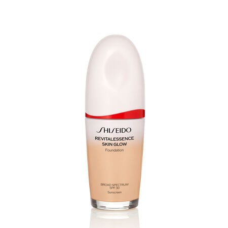An oval-shaped bottle of Shiseido Revitalessence Skin Glow Foundation SPF 30 in shade 150 Lace. The label on the bottle is white with a red accent. El texto en la etiqueta muestra el título del producto, y su protección solar.